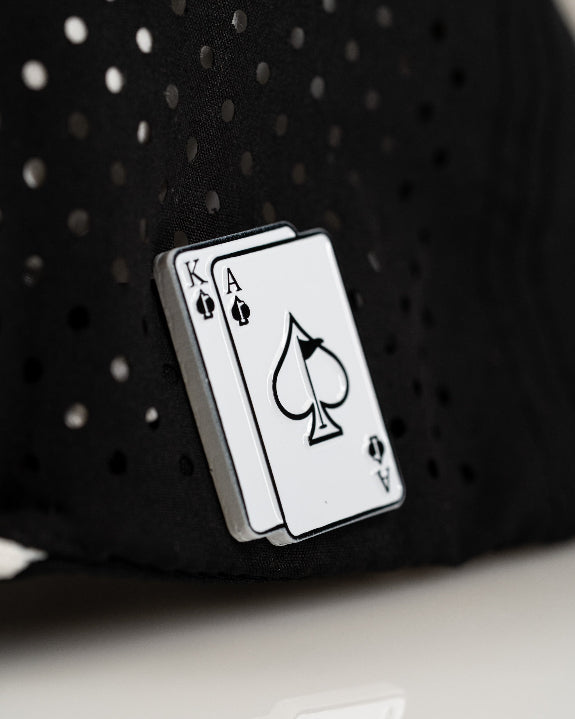 Ace/King Black perforated rope golf hat by Pins & Aces featuring a black poker-inspired design, braided rope accent, adjustable snapback, and built-in magnetic ball marker holder.