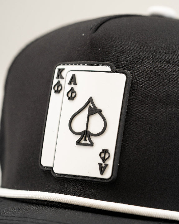 Ace/King Black perforated rope golf hat by Pins & Aces featuring a black poker-inspired design, braided rope accent, adjustable snapback, and built-in magnetic ball marker holder.