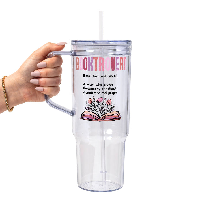 Clear glass cup with bamboo lid and straw featuring pink Booktrovert lettering, a definition about preferring fictional characters to real people, and an open book filled with pink and purple flowers.