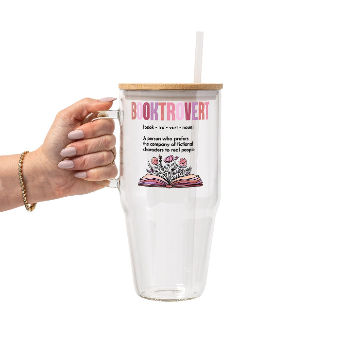 Clear glass cup with bamboo lid and straw featuring pink Booktrovert lettering, a definition about preferring fictional characters to real people, and an open book filled with pink and purple flowers.