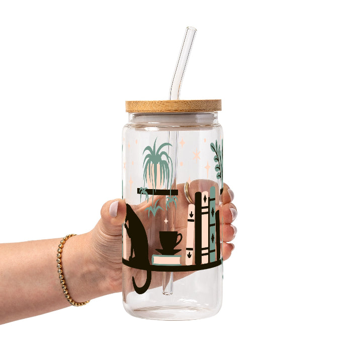 Bookish drinkware featuring a cozy wraparound bookshelf design with books, a curious kitty, and trailing green plants, available in glass cups, tumblers, and ceramic mugs.