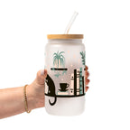 Bookish drinkware featuring a cozy wraparound bookshelf design with books, a curious kitty, and trailing green plants, available in glass cups, tumblers, and ceramic mugs.