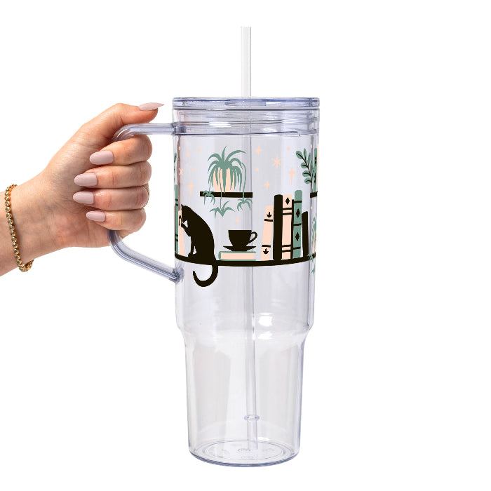 Bookish drinkware featuring a cozy wraparound bookshelf design with books, a curious kitty, and trailing green plants, available in glass cups, tumblers, and ceramic mugs.