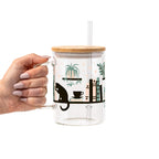 Bookish drinkware featuring a cozy wraparound bookshelf design with books, a curious kitty, and trailing green plants, available in glass cups, tumblers, and ceramic mugs.