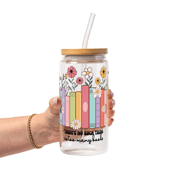 Clear glass cup with bamboo lid and straw featuring colorful pastel books surrounded by pink, yellow and white wildflowers with “There’s No Such Thing as Too Many Books” lettering.