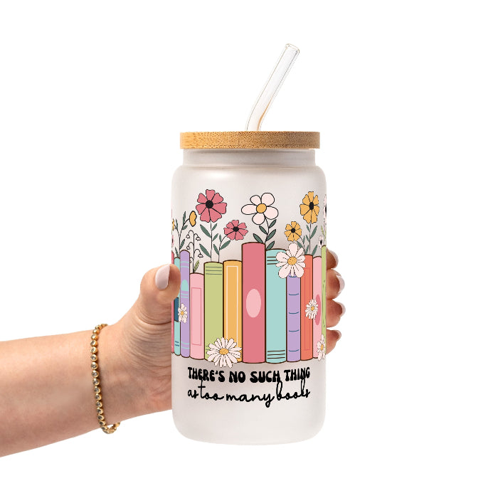 Clear glass cup with bamboo lid and straw featuring colorful pastel books surrounded by pink, yellow and white wildflowers with “There’s No Such Thing as Too Many Books” lettering.