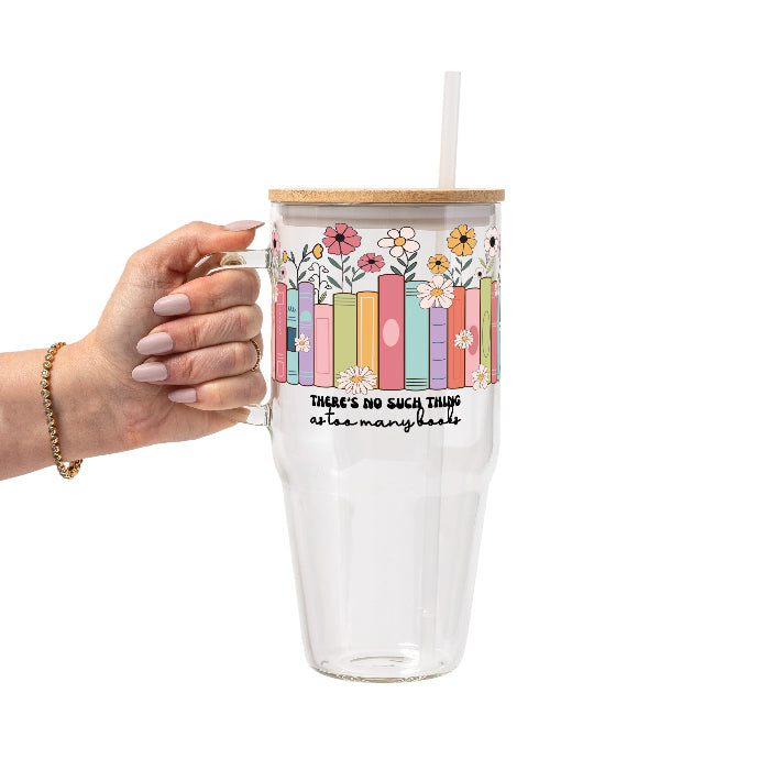 Clear glass cup with bamboo lid and straw featuring colorful pastel books surrounded by pink, yellow and white wildflowers with “There’s No Such Thing as Too Many Books” lettering.