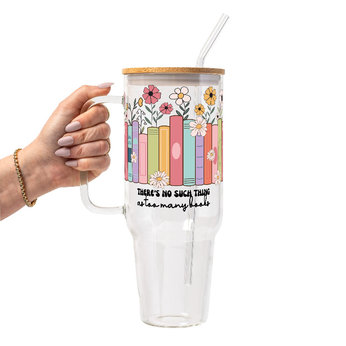 Clear glass cup with bamboo lid and straw featuring colorful pastel books surrounded by pink, yellow and white wildflowers with “There’s No Such Thing as Too Many Books” lettering.