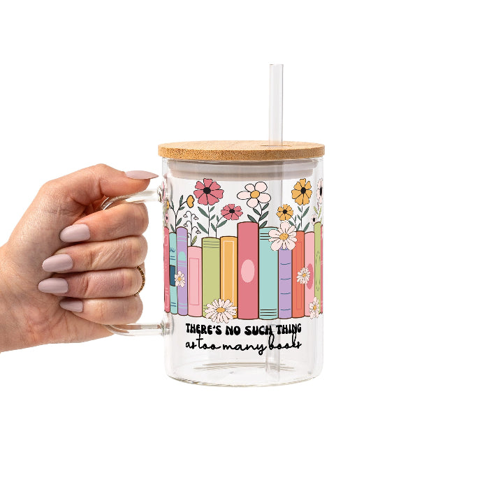 Clear glass cup with bamboo lid and straw featuring colorful pastel books surrounded by pink, yellow and white wildflowers with “There’s No Such Thing as Too Many Books” lettering.