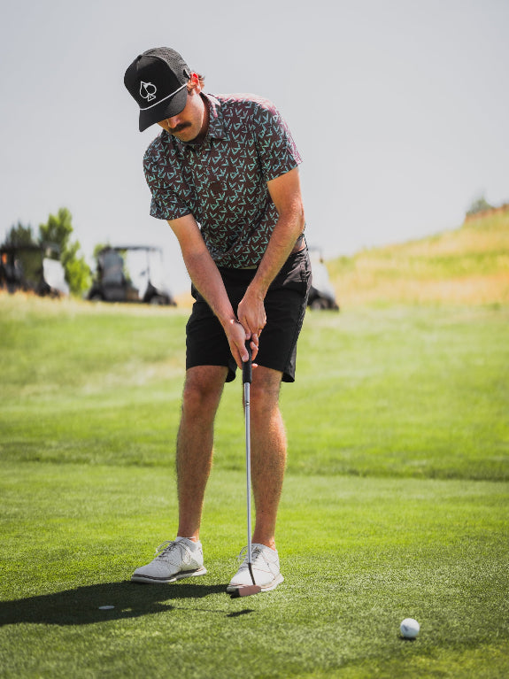 Men’s Cocoa Verde golf polo by Pins & Aces featuring a cocoa brown background with an all-over teal geometric print, short sleeves, and athletic performance fit.