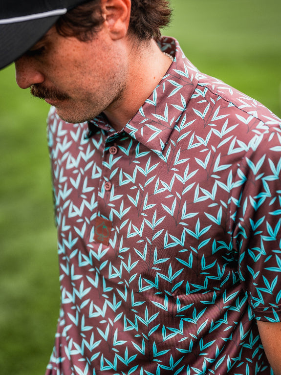 Men’s Cocoa Verde golf polo by Pins & Aces featuring a cocoa brown background with an all-over teal geometric print, short sleeves, and athletic performance fit.