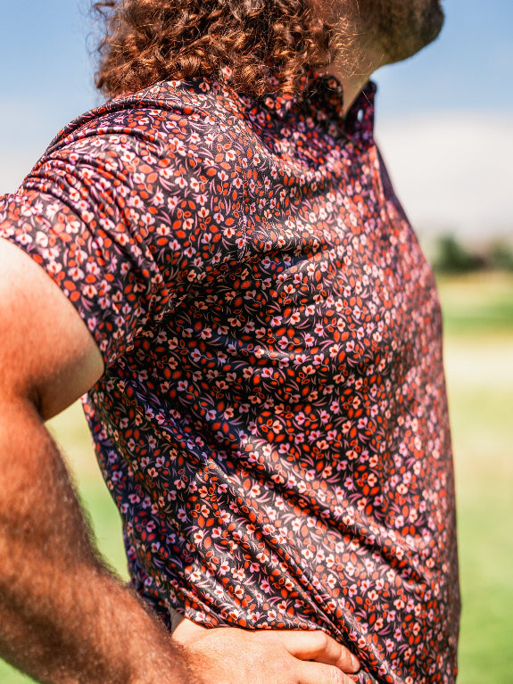 Men’s Shadow Rose golf polo by Pins & Aces featuring an all-over red and muted rose floral print on a black background with short sleeves and an athletic performance fit.