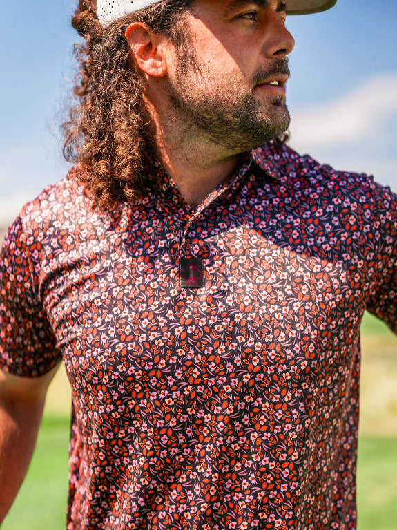 Men’s Shadow Rose golf polo by Pins & Aces featuring an all-over red and muted rose floral print on a black background with short sleeves and an athletic performance fit.