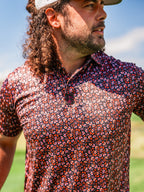 Men’s Shadow Rose golf polo by Pins & Aces featuring an all-over red and muted rose floral print on a black background with short sleeves and an athletic performance fit.