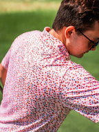 Men’s Soft Spoken golf polo by Pins & Aces featuring a subtle coral, red, navy, and white micro floral print with short sleeves and an athletic performance fit.