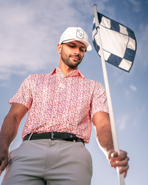 Men’s Soft Spoken golf polo by Pins & Aces featuring a subtle coral, red, navy, and white micro floral print with short sleeves and an athletic performance fit.