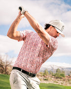 Men’s Soft Spoken golf polo by Pins & Aces featuring a subtle coral, red, navy, and white micro floral print with short sleeves and an athletic performance fit.