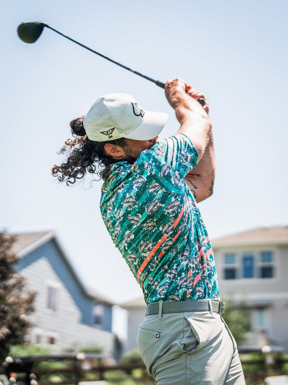 Men’s Trout Splatter golf polo by Pins & Aces featuring an all-over trout fishing print with teal, aqua, coral, and white splatter details and an athletic performance fit.