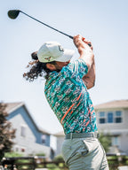 Men’s Trout Splatter golf polo by Pins & Aces featuring an all-over trout fishing print with teal, aqua, coral, and white splatter details and an athletic performance fit.