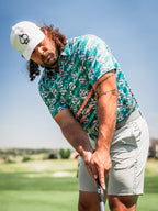 Men’s Trout Splatter golf polo by Pins & Aces featuring an all-over trout fishing print with teal, aqua, coral, and white splatter details and an athletic performance fit.