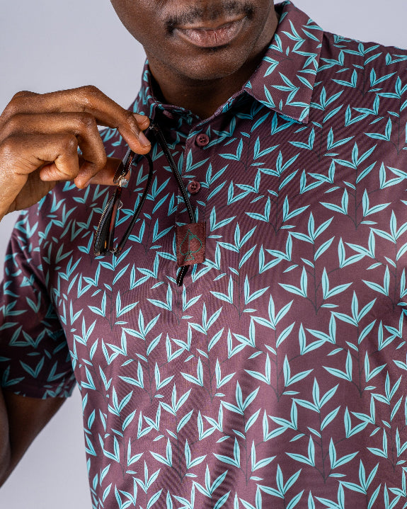 Men’s Cocoa Verde golf polo by Pins & Aces featuring a cocoa brown background with an all-over teal geometric print, short sleeves, and athletic performance fit.