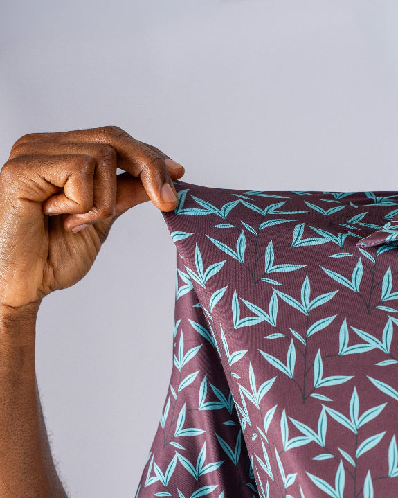 Men’s Cocoa Verde golf polo by Pins & Aces featuring a cocoa brown background with an all-over teal geometric print, short sleeves, and athletic performance fit.