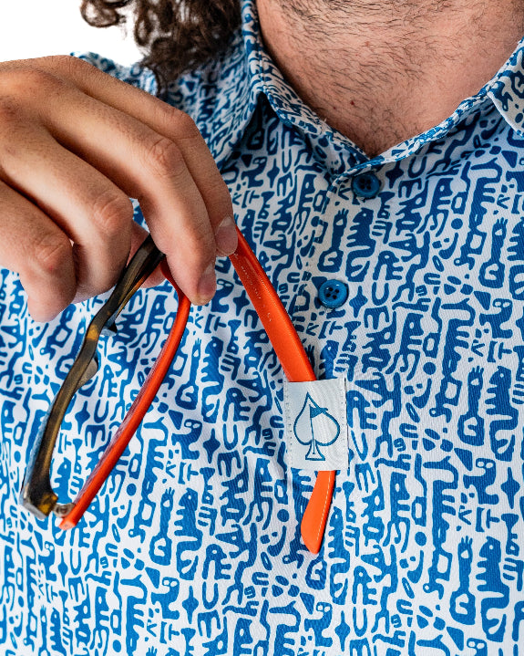 Men’s Maze Craze golf polo by Pins & Aces featuring an all-over blue maze-inspired geometric pattern with short sleeves and an athletic performance fit.