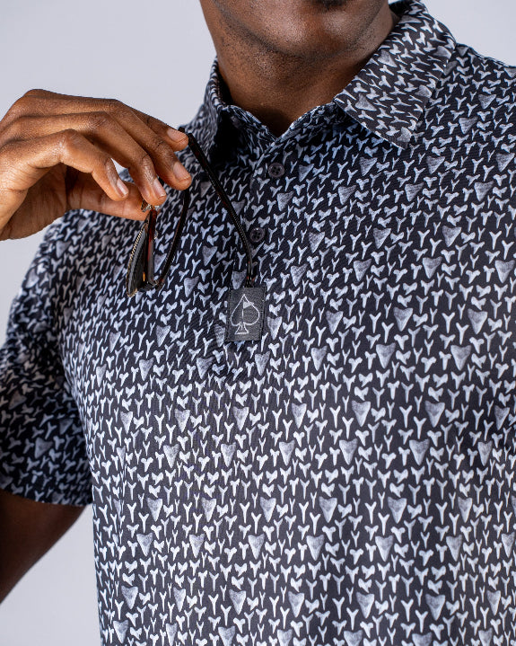 Men’s Shark Tooth golf polo by Pins & Aces featuring an all-over black, charcoal, gray, and white shark tooth-inspired micro print with short sleeves and an athletic performance fit.