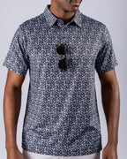 Men’s Shark Tooth golf polo by Pins & Aces featuring an all-over black, charcoal, gray, and white shark tooth-inspired micro print with short sleeves and an athletic performance fit.