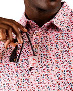 Men’s Soft Spoken golf polo by Pins & Aces featuring a subtle coral, red, navy, and white micro floral print with short sleeves and an athletic performance fit.