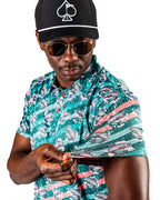 Men’s Trout Splatter golf polo by Pins & Aces featuring an all-over trout fishing print with teal, aqua, coral, and white splatter details and an athletic performance fit.