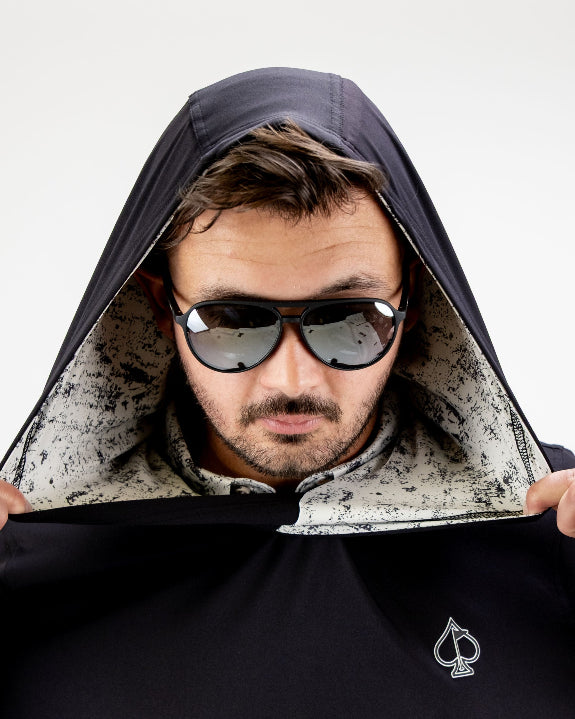Men’s White Noise Performance Golf Hoodie by Pins & Aces featuring a black lightweight stretch body, embroidered spade chest logo, long sleeves, and White Noise printed hood lining.