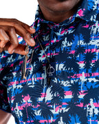 Men’s Palm Drip Dawn golf polo by Pins & Aces featuring navy palm trees over a blue, pink, and white tropical print with short sleeves and an athletic performance fit.