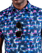 Men’s Palm Drip Dawn golf polo by Pins & Aces featuring navy palm trees over a blue, pink, and white tropical print with short sleeves and an athletic performance fit.