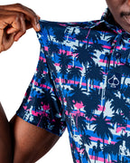 Men’s Palm Drip Dawn golf polo by Pins & Aces featuring navy palm trees over a blue, pink, and white tropical print with short sleeves and an athletic performance fit.