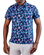 Men’s Palm Drip Dawn golf polo by Pins & Aces featuring navy palm trees over a blue, pink, and white tropical print with short sleeves and an athletic performance fit.
