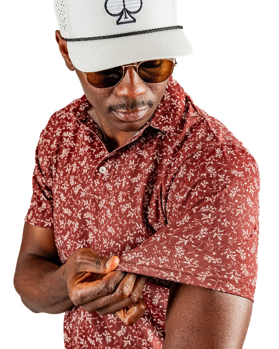 Men’s Autumn Bloom golf polo by Pins & Aces featuring a rust-colored all-over cream floral print, short sleeves, blade collar, and athletic performance fit.