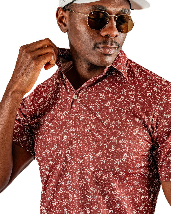 Men’s Autumn Bloom golf polo by Pins & Aces featuring a rust-colored all-over cream floral print, short sleeves, blade collar, and athletic performance fit.