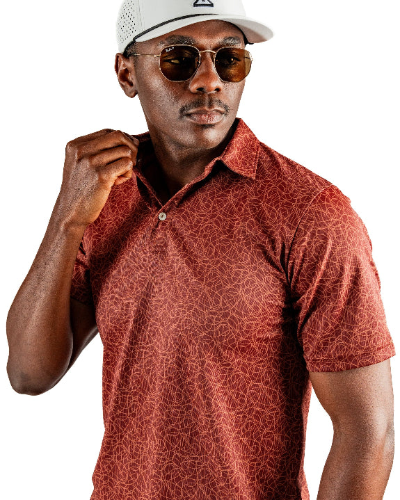 Men’s Filament golf polo by Pins & Aces featuring a rust and burnt orange abstract line pattern, short sleeves, modern blade collar, and athletic performance fit.
