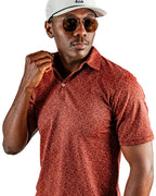 Men’s Filament golf polo by Pins & Aces featuring a rust and burnt orange abstract line pattern, short sleeves, modern blade collar, and athletic performance fit.