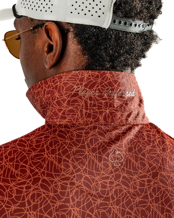 Men’s Filament golf polo by Pins & Aces featuring a rust and burnt orange abstract line pattern, short sleeves, modern blade collar, and athletic performance fit.