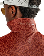 Men’s Filament golf polo by Pins & Aces featuring a rust and burnt orange abstract line pattern, short sleeves, modern blade collar, and athletic performance fit.