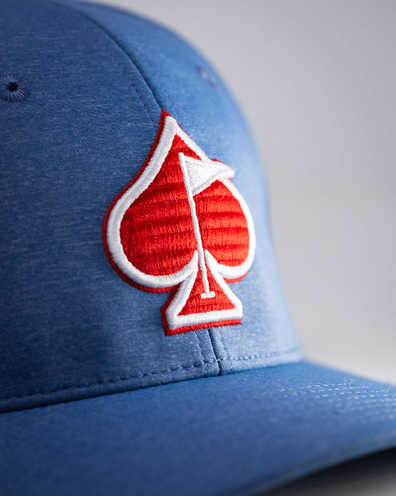 Blue Performance Spade golf hat by Pins & Aces featuring an embroidered Fairway Wave Spade logo, adjustable snapback, curved bill, and built-in magnetic golf ball marker holder.