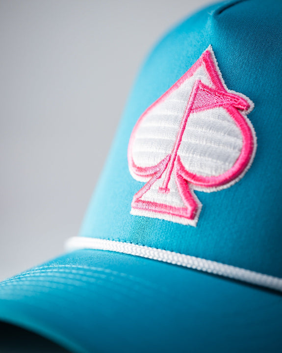 Baby blue perforated rope golf hat by Pins & Aces featuring a pink and white embroidered Fairway Wave Spade logo, white rope accent, perforated panels, and curved bill.