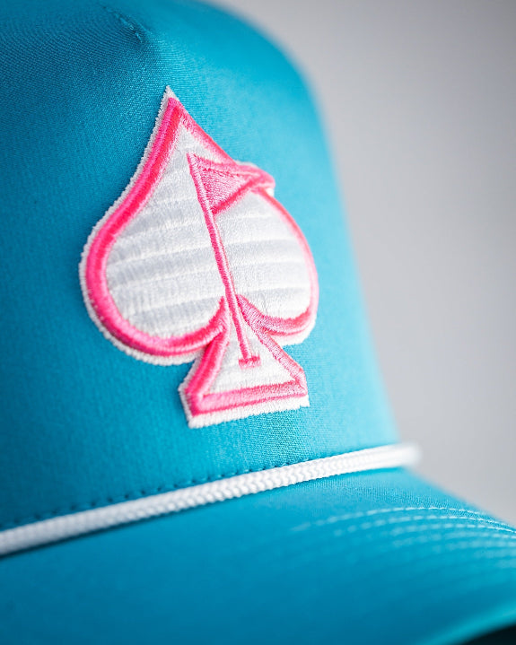 Baby blue perforated rope golf hat by Pins & Aces featuring a pink and white embroidered Fairway Wave Spade logo, white rope accent, perforated panels, and curved bill.