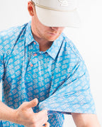 Men’s Skyline Dash Blue golf polo by Pins & Aces featuring a bright blue geometric dash pattern with pink accents and an athletic performance fit.