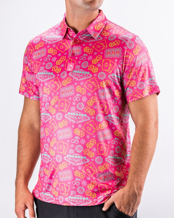 Men’s Big Ace Fuchsia golf polo by Pins & Aces featuring a bright pink casino print with playing cards, dice, poker chips, slot machines, and an athletic performance fit.