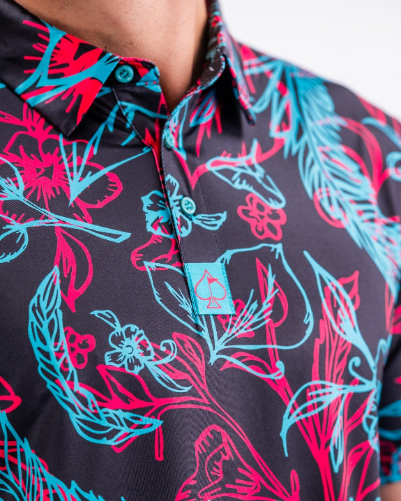 Men’s Cabo Electric golf polo by Pins & Aces featuring an aqua, hot pink, and coral tropical floral and leaf print on a dark charcoal background with an athletic performance fit.