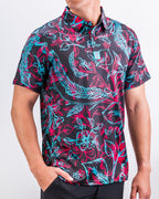 Men’s Cabo Electric golf polo by Pins & Aces featuring an aqua, hot pink, and coral tropical floral and leaf print on a dark charcoal background with an athletic performance fit.