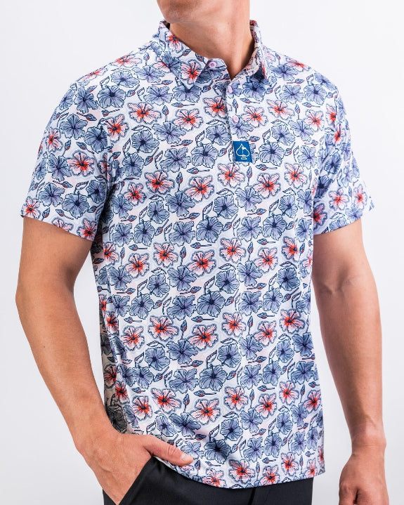 Men’s Hibiscus Harmony golf polo by Pins & Aces featuring blue and coral hibiscus flowers on a white lightweight performance golf shirt.